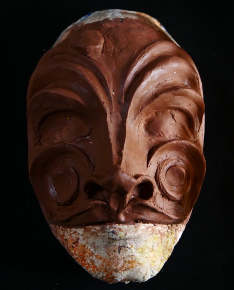 Masque sculpté en terre cuite avec des motifs distinctifs et un fond noir.